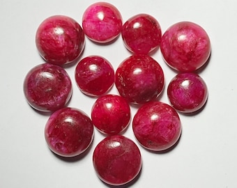 May include: A collection of eleven polished, round gemstones in varying shades of red. The stones have a smooth, reflective surface, with a marbled appearance. The gemstones are arranged on a white surface, showcasing their color and texture.