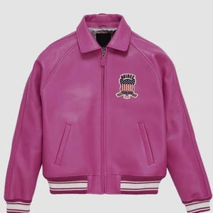 Può includere: Giacca in pelle fucsia con zip, colletto e polsini e orlo a coste. La giacca presenta una toppa sul petto con la scritta "AVIREX" e un disegno che incorpora la bandiera americana. Due tasche anteriori.