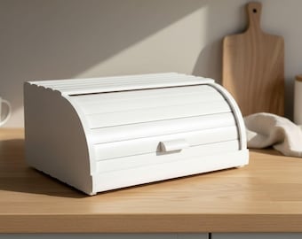 Può includere: Un portapane bianco con coperchio a serrandina e una piccola maniglia rettangolare. Il contenitore presenta un design a doghe orizzontali sullo sportello anteriore e una finitura liscia e solida sui pannelli laterali per la conservazione.
