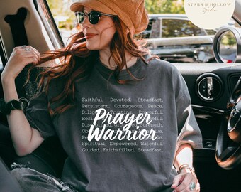May include: A gray t-shirt with the words "Prayer Warrior" in a stylized font. The shirt also features a list of words such as "Faithful", "Devoted", and "Steadfast". The image includes the text "SVG & PNG DOWNLOAD".
