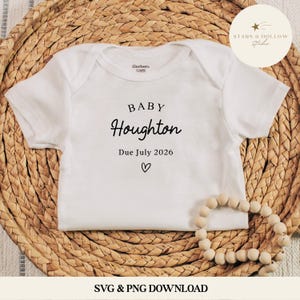 May include: White baby bodysuit with the text "BABY Houghton Due July 2026" and a heart symbol. The bodysuit is on a woven wicker surface with a wooden bead garland. The brand name "Gerber" is visible on the bodysuit.