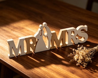 Könnte beinhalten: Ein dekoratives Holzschild mit dem Schriftzug MR und MRS und einer ausgeschnittenen Silhouette eines Paares zwischen den Buchstaben. Die Buchstaben sind weiß mit naturfarbenen Holzkanten, die Silhouette des Paares ist weiß mit Holzkanten.