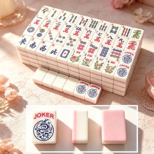 May include: A set of white Mahjong tiles with pink backs, featuring various red, blue, and green engraved characters, numbers, and symbols. The tiles include suits, winds, dragons, flowers, seasons, and Joker tiles with a blue dragon graphic.