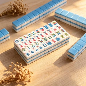 May include: A set of white and light blue mahjong tiles arranged in rows and a central stack. The tiles feature various colorful Chinese characters, numbers, and symbols in red, green, and blue ink, including circles, bamboo, and directional markers.