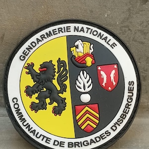 Puede incluir: Un parche redondo con las palabras "GENDARMERIE NATIONALE" y "COMMUNAUTE DE BRIGADES D'ISBERGUES". El parche presenta un león negro sobre fondo amarillo y otros emblemas en rojo, blanco y negro.