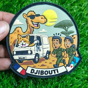 Op de afbeelding: Een ronde patch met een kameel met zonnebril, een kat in een busje en twee mensen in militaire uniformen die rennen. De patch heeft het woord "DJIBOUTI" en de vlag van Djibouti.