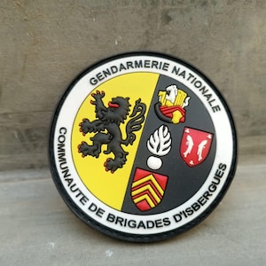 K&ouml;nnte beinhalten: Ein runder Aufn&auml;her mit den Worten "Gendarmerie Nationale" und "Communaut&eacute; de Brigades d'Isbergues". Der Aufn&auml;her zeigt einen schwarzen L&ouml;wen, ein Schild und andere Embleme in Gelb, Rot und Wei&szlig;.