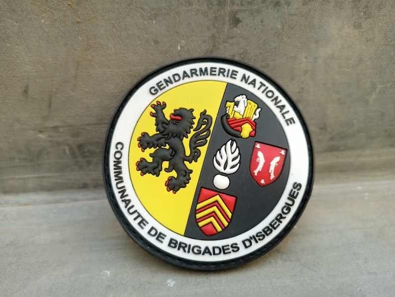K&ouml;nnte beinhalten: Ein runder Aufn&auml;her mit den Worten "Gendarmerie Nationale" und "Communaut&eacute; de Brigades d'Isbergues". Der Aufn&auml;her zeigt einen schwarzen L&ouml;wen, ein Schild und andere Embleme in Gelb, Rot und Wei&szlig;.