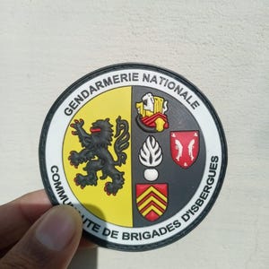 K&ouml;nnte beinhalten: Ein runder Aufn&auml;her mit den Worten "Gendarmerie Nationale" und "Communaute de Brigades d'Isbergues". Der Aufn&auml;her hat einen schwarzen Rand und ein Design mit einem schwarzen L&ouml;wen, einem rot-gelben Wappen und anderen Emblemen.