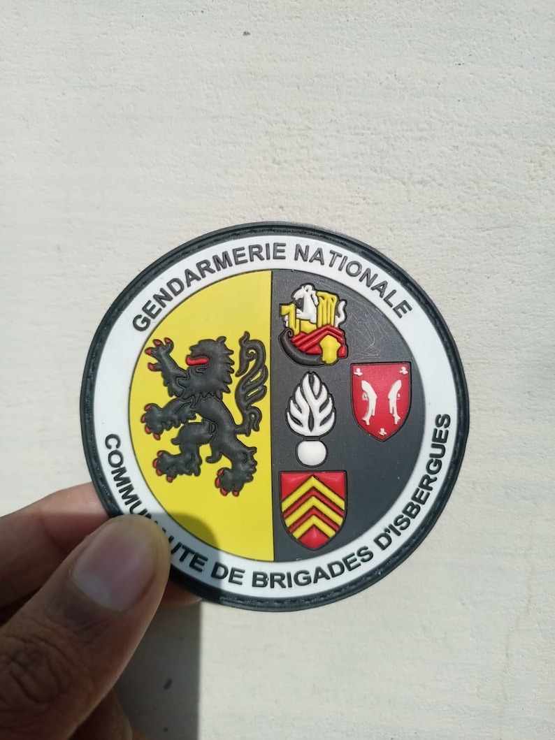 K&ouml;nnte beinhalten: Ein runder Aufn&auml;her mit den Worten "Gendarmerie Nationale" und "Communaute de Brigades d'Isbergues". Der Aufn&auml;her hat einen schwarzen Rand und ein Design mit einem schwarzen L&ouml;wen, einem rot-gelben Wappen und anderen Emblemen.