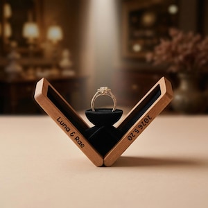 May include: A gold engagement ring with a diamond flower design sits in an open wooden box with black velvet lining. The box is engraved with "Luna & Rae" and "2026.5.20". The ring is centered on a black velvet stand.