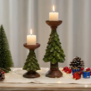 Puede incluir: Dos candelabros con forma de árbol de Navidad con velas blancas encendidas. Los candelabros son verdes con detalles marrones. También se ven un pequeño árbol de Navidad, una piña y regalos envueltos, sugiriendo un tema festivo.