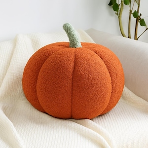 Puede incluir: Un cojín decorativo con forma de calabaza naranja con un tallo verde. El cojín tiene una superficie texturizada y afelpada, diseñado para parecerse a una calabaza real. Perfecto para la decoración de otoño, añade un toque otoñal a cualquier habitación.