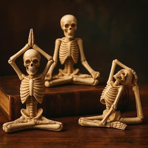 Op de afbeelding: Drie beige skeletbeeldjes in yogahoudingen. Eén skelet heeft de handen boven het hoofd, een ander zit in een zittende meditatiehouding en de derde is achterover gebogen. De beeldjes staan op een donker houten oppervlak.