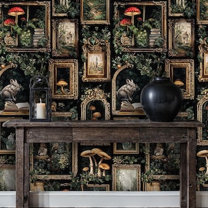 Moody dark academia wallpaper with ornate framed forest art and mushrooms styled behind a wooden console table with candle and ceramic decor, creating a dramatic vintage interior vignette.