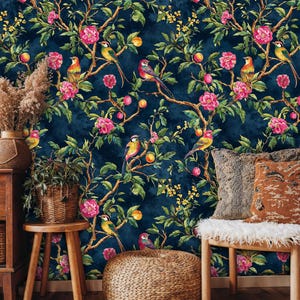 Cozy living room with navy blue chinoiserie wallpaper showing birds and floral branches. Natural wood accents, a rattan chair, pampas grass, and textured cushions enhance the bold botanical mural, blending vintage charm with modern bohemian style.