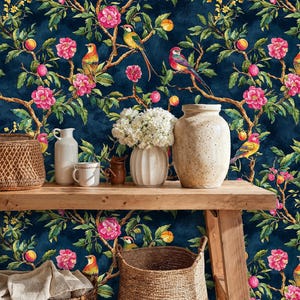 Entryway interior styled with a navy chinoiserie wallpaper featuring colorful birds, blooming pink flowers, and fruit branches. The vibrant mural contrasts with rustic wooden furniture, wicker baskets, and ceramic vases, creating a warm and elegant botanical look.