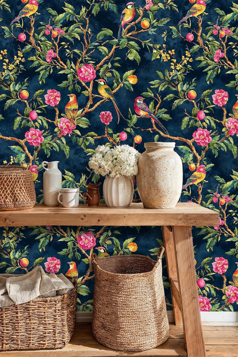 Entryway interior styled with a navy chinoiserie wallpaper featuring colorful birds, blooming pink flowers, and fruit branches. The vibrant mural contrasts with rustic wooden furniture, wicker baskets, and ceramic vases, creating a warm and elegant botanical look.
