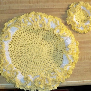 May include: A set of two crocheted doilies in yellow and white. The larger doily has a ruffled edge and the smaller doily is a simple circle.