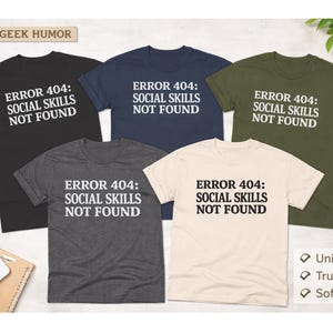 May include: Five t-shirts in black, navy, charcoal, cream, and olive green, each with the text "ERROR 404: SOCIAL SKILLS NOT FOUND" in white. The phrase "FUNNY GEEK HUMOR" is at the top. Features include unisex fit, true to size, and soft cotton.