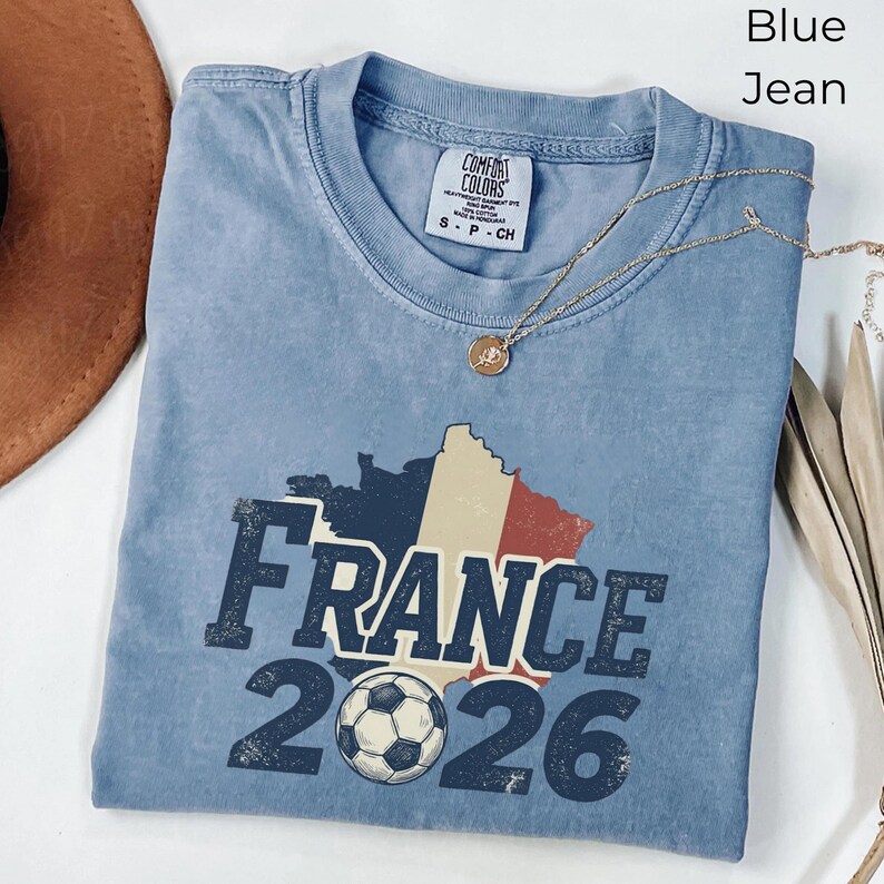 Vintage France 2026 soccer t-shirt in Blue Jean color. Comfort Colors garment-dyed tee mockup featuring distressed retro France football text, soccer ball, and French map design. Premium world cup soccer fan clothing.