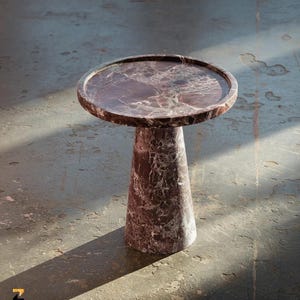 May include: A round marble side table with a dark red and white veined pattern. The table has a circular top with a raised edge and a conical base. The table is approximately 20 inches in diameter and 24 inches tall.