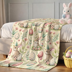 May include: A cream-colored Easter-themed blanket draped over a bed, featuring a repeating pattern of bunnies, eggs, and flowers in pastel colors. A plush bunny and a basket of decorated eggs are also present.