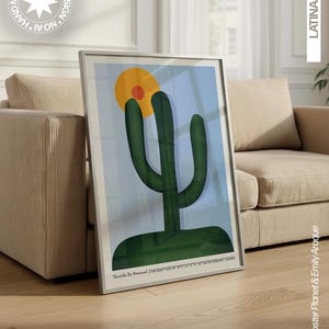 May include: A framed art print featuring a stylized dark green cactus against a light blue background with a large yellow sun and a smaller orange circle. The bottom of the print includes the text Tarsila Do Amaral and additional small text.