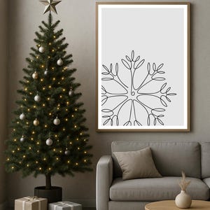 Könnte beinhalten: Eine weihnachtliche Szene mit einem geschmückten Weihnachtsbaum, einem gerahmten Schneeflocken-Kunstdruck und verpackten Geschenken. Ein graues Sofa und ein Holztisch ergänzen das gemütliche Interieur.