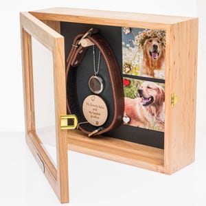 Pu&ograve; includere: Una scatola commemorativa in legno per animali domestici con porta in vetro, che mostra un collare per cani in pelle marrone, un ciondolo e due foto di un golden retriever. Il ciondolo recita "My favorite hello and my hardest goodbye."