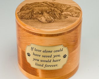 May include: A wooden pet urn with a detailed engraved image of a long-haired dachshund on the lid. The urn has a gold plaque with the text "If love alone could have saved you, you would have lived forever." The name "Ebby" is engraved on the lid.