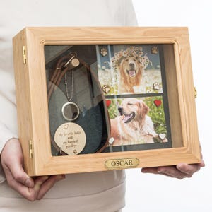 May include: A wooden pet memorial shadow box with a glass front. Inside are two photos of a golden retriever, a brown leather collar, and a pendant. The box has the name "OSCAR" on a small plaque.