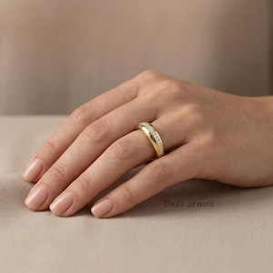 Puede incluir: Un anillo de oro con un diseño curvo, engastado con pequeñas piedras brillantes. El anillo está en el dedo de una persona, mostrando su superficie pulida y su estilo elegante. Es una pieza de joyería.