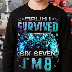 May include: Black sweatshirt with a blue and teal video game controller graphic. Text on the shirt reads "BRUH I SURVIVED SIX-SEVEN I'M 8". The design includes stars and geometric shapes.