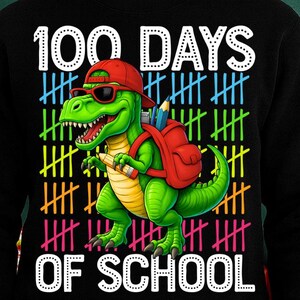 May include: Black sweatshirt with a colourful graphic celebrating 100 days of school. The design features a green dinosaur wearing a red cap and sunglasses, carrying a red backpack and pencil. The text "100 DAYS OF SCHOOL" is displayed in white.