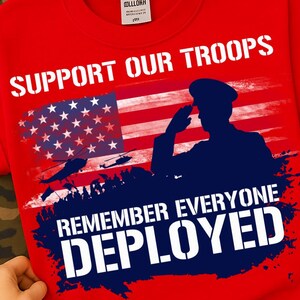 Könnte beinhalten: Rotes Rundhals-T-Shirt mit patriotischem Design. Das Shirt zeigt den Text "SUPPORT OUR TROOPS" über einer amerikanischen Flagge und einer Silhouette eines salutierenden Soldaten. Darunter steht der Text "REMEMBER EVERYONE DEPLOYED".