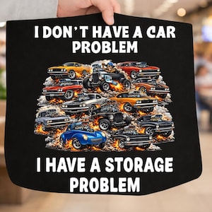 May include: Black tote bag with the text "I DON'T HAVE A CAR PROBLEM I HAVE A STORAGE PROBLEM" and a graphic of various hot rod cars in shades of orange, red, blue, and black.