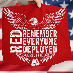 May include: Red tote bag featuring a white eagle graphic with outstretched wings and the American flag incorporated. The text reads "REMEMBER EVERYONE DEPLOYED EST. 1776" in white. Includes two dog tags.