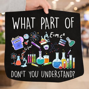 May include: Black tote bag with the text "WHAT PART OF DON'T YOU UNDERSTAND?" and science-themed illustrations. The design includes beakers, a microscope, and the formula E=mc². The bag is held by a person.