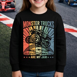 May include: Black sweatshirt with a colorful graphic featuring a monster truck, tire tracks, and cars. Text reads "MONSTER TRUCKS ARE MY JAM" in a retro style. The design has a vintage, distressed look.