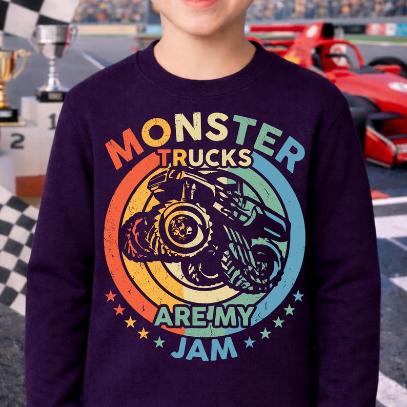 May include: A dark purple sweatshirt featuring a colorful graphic of a monster truck inside a circle with the words "MONSTER TRUCKS ARE MY JAM". The design uses orange, yellow, green, and blue colors. Stars surround the bottom of the graphic.
