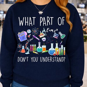 Może przedstawiać: Granatowa bluza z napisem "WHAT PART OF DON'T YOU UNDERSTAND?" oraz grafiką o tematyce naukowej. Grafika zawiera zlewki, prob&oacute;wki i wzory naukowe, takie jak E=mc&sup2;.