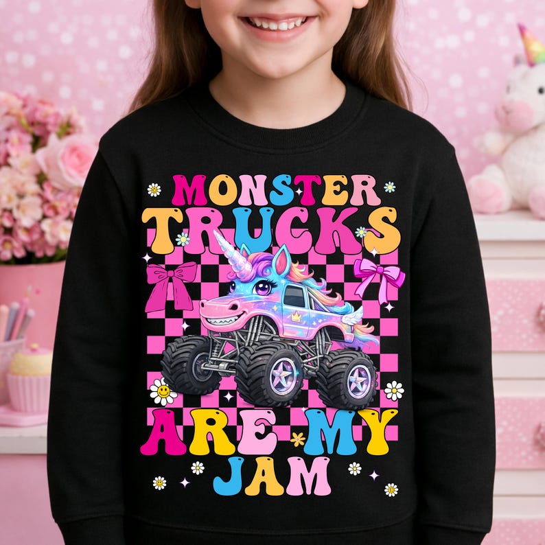 May include: Black sweatshirt featuring a colorful graphic of a monster truck with a unicorn horn, set against a pink and black checkered background. The text "MONSTER TRUCKS ARE MY JAM" is displayed in vibrant colors.