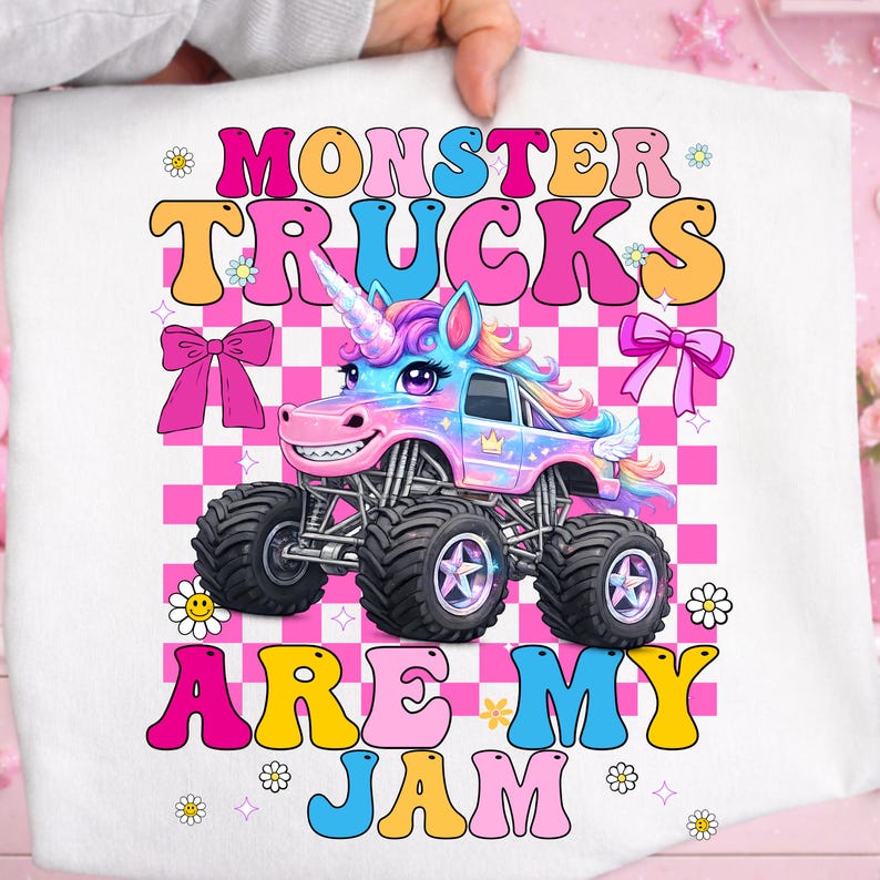 May include: A white graphic tee featuring a colorful monster truck designed as a unicorn. The text "MONSTER TRUCKS ARE MY JAM" is displayed in a retro font with pink, orange, yellow, and blue colors. The background is a pink and white checkered pattern.