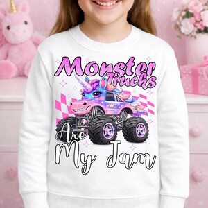 Puede incluir: Sudadera blanca con un gr&aacute;fico colorido de un cami&oacute;n monstruo dise&ntilde;ado como un unicornio. El texto "Monster Trucks Are My Jam" se muestra en una fuente l&uacute;dica. El dise&ntilde;o incluye tonos rosas, morados y azules, con un fondo a cuadros.