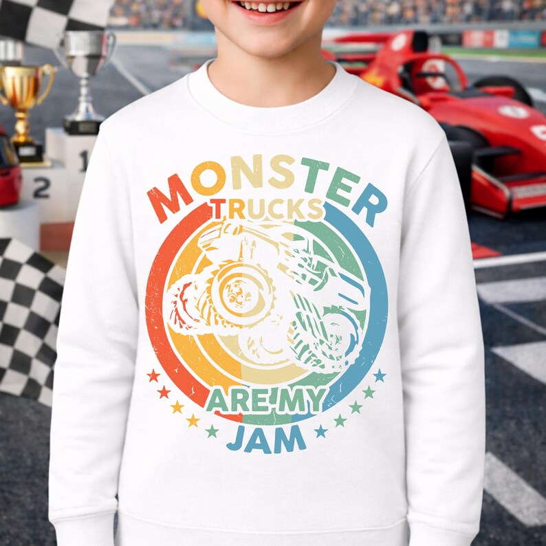 May include: White sweatshirt with a colorful graphic that says "MONSTER TRUCKS ARE MY JAM." The design features a monster truck illustration inside a circular rainbow design with stars. The sweatshirt is worn by a person.