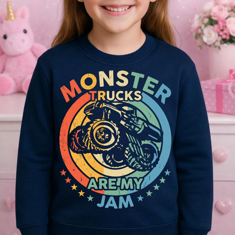 May include: Navy blue sweatshirt featuring a colorful graphic of a monster truck inside a circular design. The text reads "MONSTER TRUCKS ARE MY JAM" in a rainbow color scheme. The design includes stars and a vintage aesthetic.