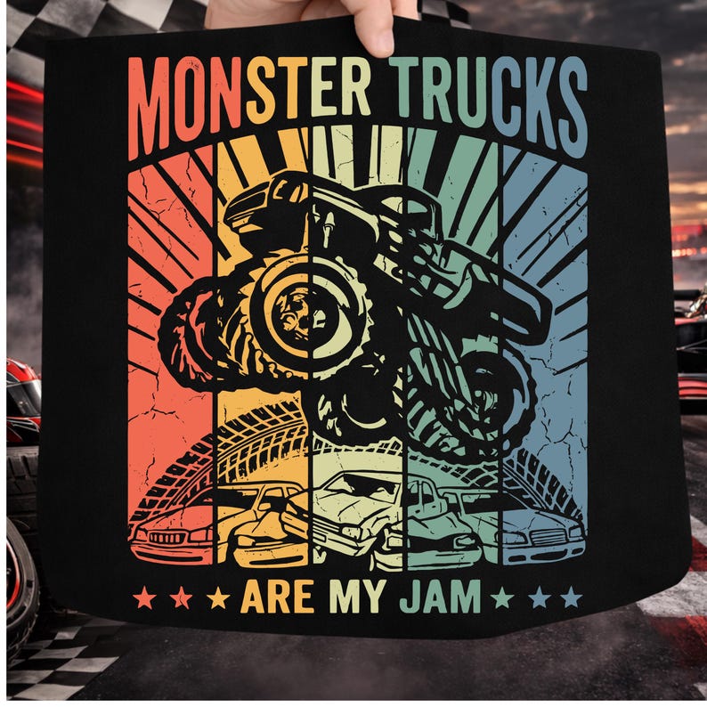 May include: Black graphic featuring a monster truck in mid-air, with the text "MONSTER TRUCKS ARE MY JAM." The design uses a retro color palette of orange, yellow, green, and blue, with a distressed effect. Below the truck are illustrations of cars.