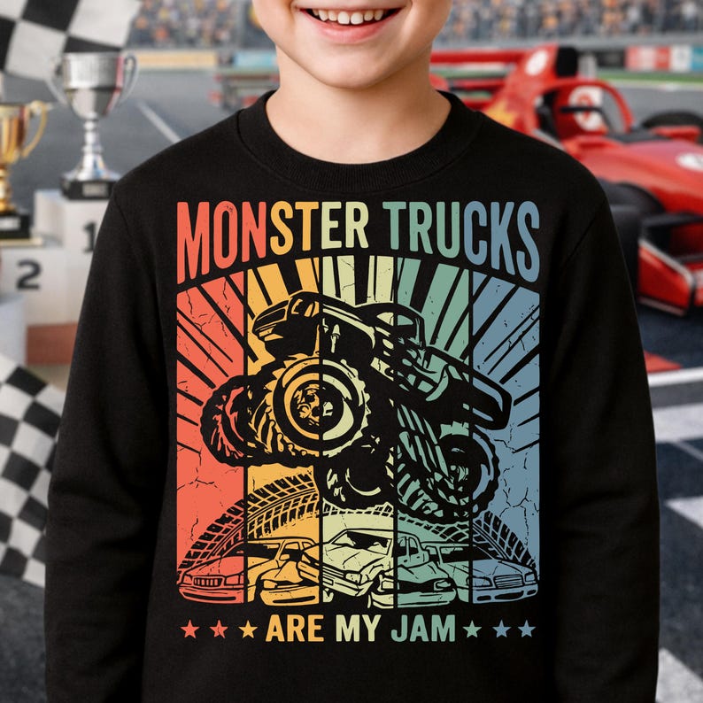 May include: Black sweatshirt with a colorful graphic that says "MONSTER TRUCKS ARE MY JAM." The design features a monster truck jumping, with tire tracks and car silhouettes below. The background has a retro sunset design.