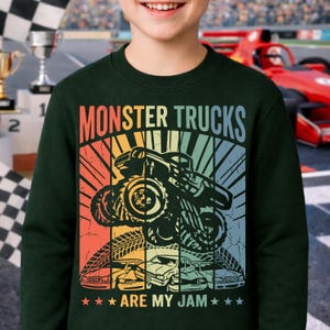 May include: Dark green sweatshirt with a colorful graphic that says "MONSTER TRUCKS ARE MY JAM." The graphic features a monster truck, tire tracks, and several cars in a retro style.